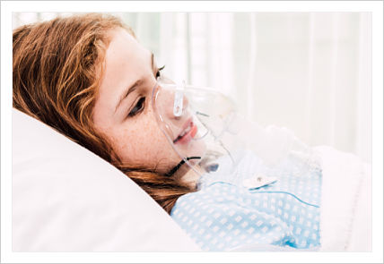 A young girl is lying in a hospital bed and has a mask covering her nose and mouth