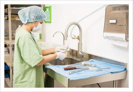 A women fully dressed in medical attire is washing and rinsing surgical tools.