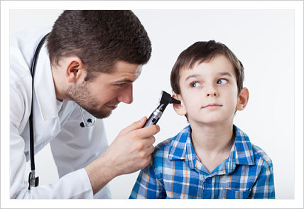 A male doctor is holding an otoscope and examining a young boys ear.