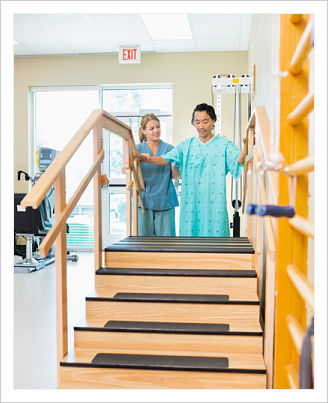 A female physical therapist is assisting a male patient up and down the stairs